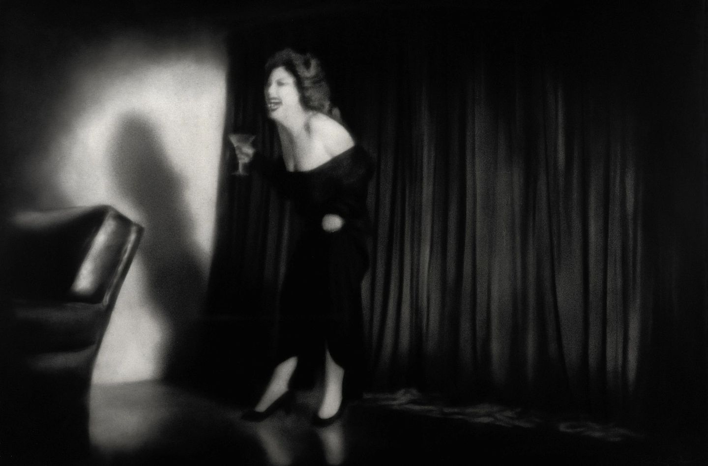 A woman in black dress on stage with curtains.