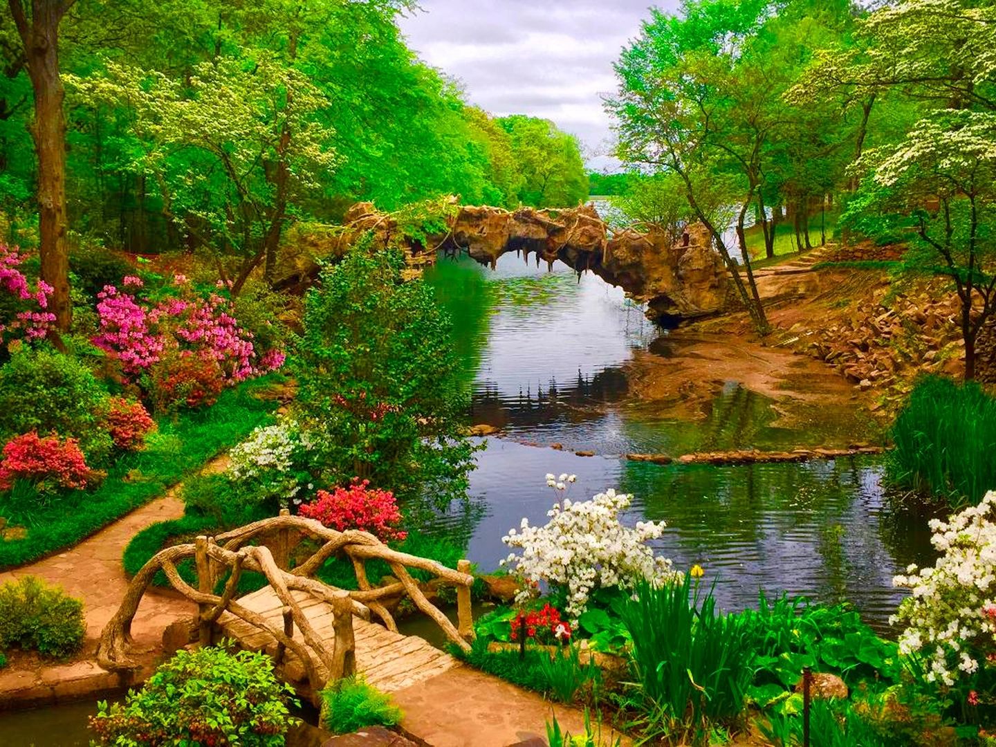 A bridge over water surrounded by trees and flowers.