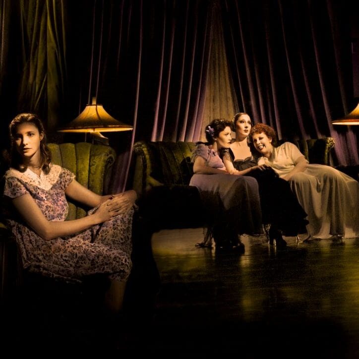 Four women in evening gowns in a dimly lit room.